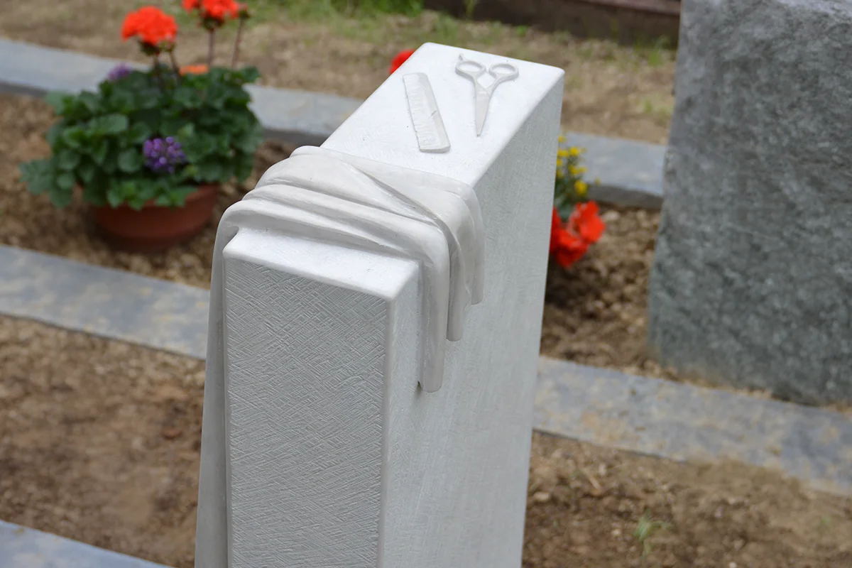 Grabstein mit individueller Verzierung mit einer Schere und einem Handtuch aus Stein